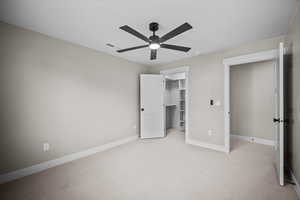 Unfurnished bedroom featuring light colored carpet, a walk in closet, and a ceiling fan