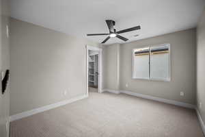 Unfurnished bedroom with a walk in closet, carpet, and a ceiling fan