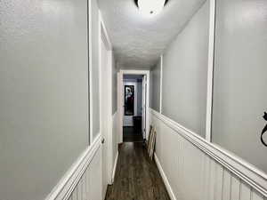 Corridor featuring dark wood finished floors, a wainscoted wall, a textured ceiling, and a decorative wall
