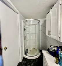 Full bathroom featuring a textured ceiling, vanity, a shower stall, marble finish floors, and tile walls