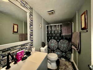 Bathroom with vanity, a shower stall, backsplash, and a textured ceiling
