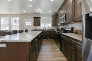 Kitchen with stainless steel appliances, dark brown cabinets, recessed lighting, a kitchen island, and light stone countertops