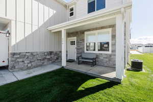 Doorway to property featuring stone siding, board and batten siding, covered porch, and a lawn