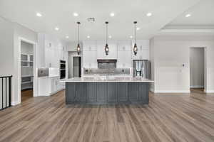 Kitchen with white cabinetry, decorative light fixtures, a large island with sink, recessed lighting, and tasteful backsplash