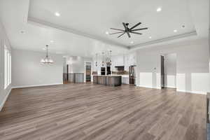 Unfurnished living room with a tray ceiling, light wood-style flooring, recessed lighting, and a ceiling fan