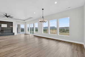 Unfurnished living room featuring light wood finished floors, a chandelier, recessed lighting, a ceiling fan, and a tray ceiling