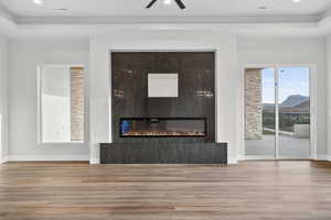 Unfurnished living room featuring a raised ceiling, wood finished floors, a fireplace, recessed lighting, and ceiling fan