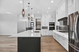 Kitchen with decorative backsplash, stainless steel appliances, hanging light fixtures, light wood-style floors, and white cabinets