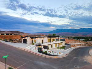 View of front of property with a mountain view, concrete driveway, stone siding, a garage, and a balcony