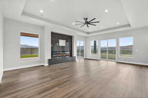 Unfurnished living room with a tray ceiling, a glass covered fireplace, wood finished floors, recessed lighting, and a ceiling fan