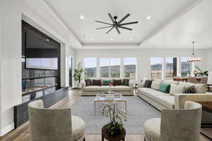 Living room with wood finished floors, a tray ceiling, a chandelier, a high end fireplace, and recessed lighting
