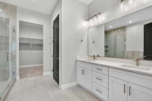 Bathroom with a shower stall, double vanity, a walk in closet, recessed lighting, and light tile patterned flooring