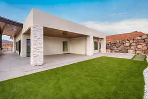 Rear view of house featuring stone siding, stucco siding, a patio, a yard, and a mountain view
