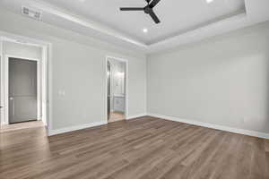 Unfurnished bedroom featuring a raised ceiling, recessed lighting, light wood finished floors, a ceiling fan, and ensuite bathroom
