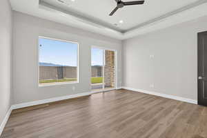 Empty room with a tray ceiling, light wood-type flooring, recessed lighting, and a ceiling fan