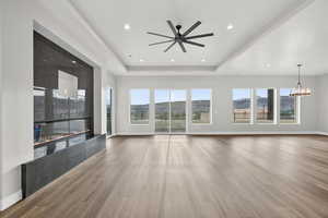 Unfurnished living room with wood finished floors, a raised ceiling, a chandelier, ceiling fan, and recessed lighting