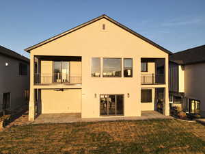 Rear view of house featuring a balcony, a lawn, and stucco siding