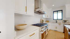 Kitchen featuring white cabinetry, stainless steel appliances, wall chimney exhaust hood, light wood-style flooring, and recessed lighting