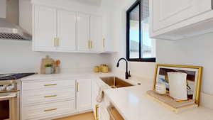 Kitchen with wall chimney range hood, stainless steel stove, white cabinetry, and light stone countertops
