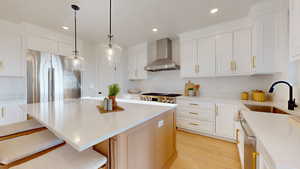 Kitchen featuring light wood-style floors, a center island, light stone counters, wall chimney exhaust hood, and white cabinetry