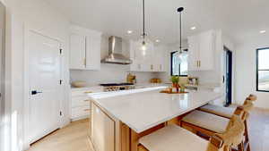 Kitchen with wall chimney exhaust hood, light stone countertops, a center island, a kitchen breakfast bar, and light wood-style flooring