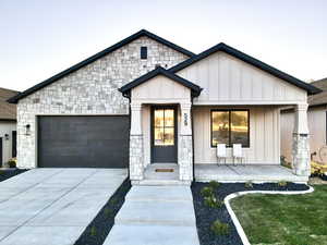 View of front of home featuring a garage, board and batten siding, stone siding, concrete driveway, and covered porch