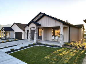View of front of home featuring driveway, a front lawn, covered porch, an attached garage, and board and batten siding