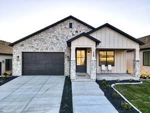 View of front facade with board and batten siding, a garage, concrete driveway, stone siding, and covered porch