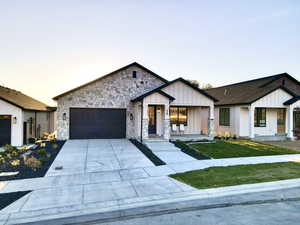 View of front of house with board and batten siding, a garage, concrete driveway, a front lawn, and stone siding