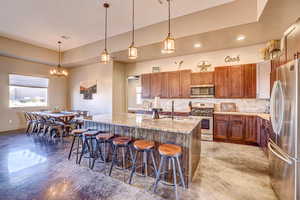 Kitchen featuring backsplash, pendant lighting, a kitchen bar, appliances with stainless steel finishes, and recessed lighting
