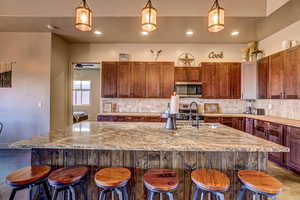 Kitchen with decorative light fixtures, a kitchen bar, backsplash, a kitchen island with sink, and recessed lighting