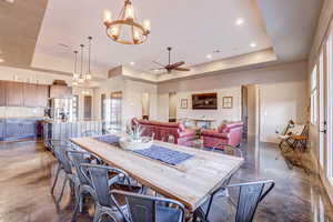 Dining room with a raised ceiling, ceiling fan, a chandelier, finished concrete floors, and recessed lighting