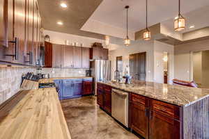 Kitchen with concrete floors, butcher block countertops, decorative light fixtures, backsplash, and an island with sink