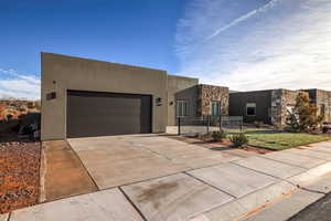 Pueblo-style house with an attached garage, concrete driveway, stucco siding, and stone siding