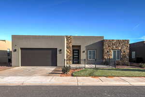 View of front of property featuring an attached garage, stone siding, driveway, stucco siding, and a porch