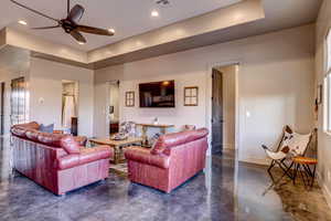 Living area with finished concrete flooring, a ceiling fan, a tray ceiling, and recessed lighting