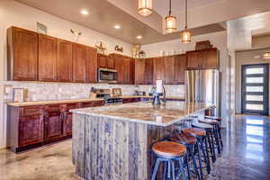 Kitchen with backsplash, light stone counters, pendant lighting, a breakfast bar area, and a large island