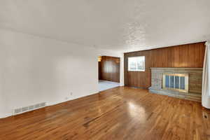 Unfurnished living room featuring wooden walls, wood finished floors, a stone fireplace, and a textured ceiling