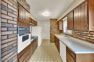 Kitchen featuring brick wall, white appliances, light countertops, light flooring, and brown cabinets