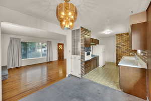 Kitchen featuring light countertops, brown cabinetry, light flooring, a chandelier, and white appliances