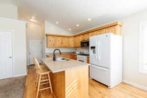 Kitchen with white appliances, light brown cabinetry, light stone countertops, light wood-type flooring, and a center island with sink