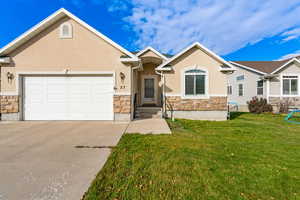 View of front facade featuring stone siding, a front lawn, stucco siding, driveway, and an attached garage
