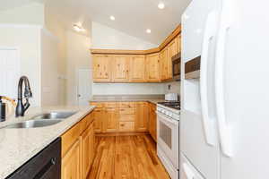 Kitchen with white appliances, light brown cabinets, light wood-style flooring, vaulted ceiling, and light stone counters