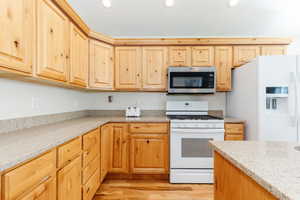 Kitchen featuring white appliances, light stone counters, light wood finished floors, light brown cabinetry, and recessed lighting
