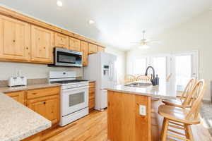 Kitchen with white appliances, vaulted ceiling, light stone countertops, light wood-type flooring, and light brown cabinetry