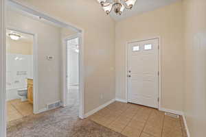 Foyer featuring light tile patterned floors, light colored carpet, a chandelier, and ceiling fan