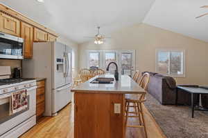 Kitchen with a ceiling fan, white gas stove, a kitchen bar, dark stone counters, and vaulted ceiling