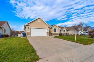 View of front of house with a front lawn, concrete driveway, stucco siding, and stone siding