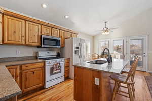 Kitchen with white appliances, light stone countertops, a center island with sink, vaulted ceiling, and light wood finished floors