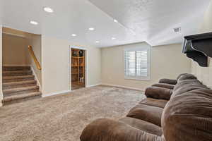 Living room with light colored carpet, recessed lighting, a textured ceiling, and stairs